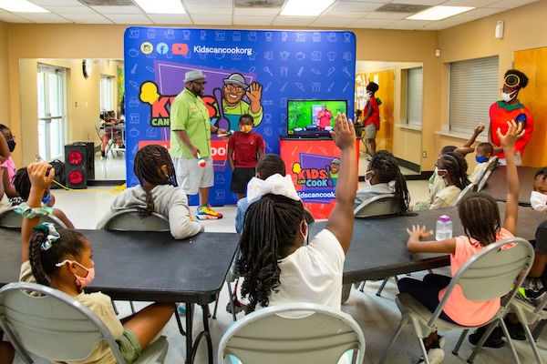 A classroom with a big banner and kids raising their hands